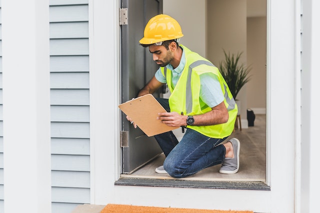 a home inspector in a yellow hard hat and reflective vest checking a doorway